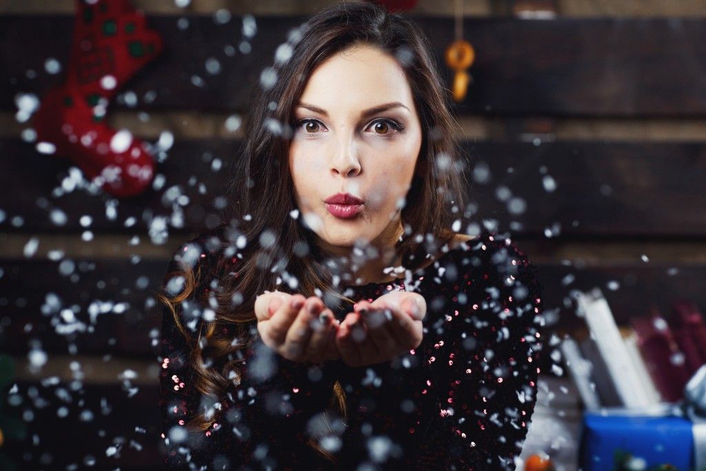 Pretty girl blows snow from her palms standing in room prepared for Christmas holidays
